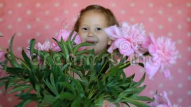 小女孩藏在一束牡丹花里。 宝宝玩粉色牡丹花